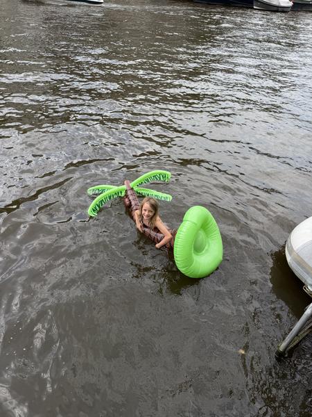 A young child joyfully plays in the water of Oudeschans, Uilenburg, Amsterdam, floating on a palm tree-shaped inflatable and a bright green ring